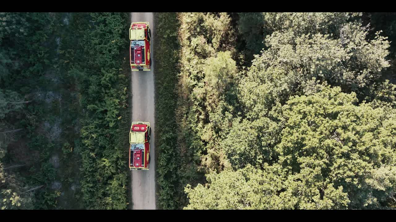 Des véhicules de pompiers traversent une route forestière, prise de vue aérienne extraite du reportage